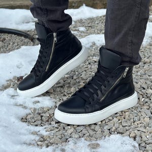 May include: A pair of black leather high-top trainers with white soles and a zip detail on the side.