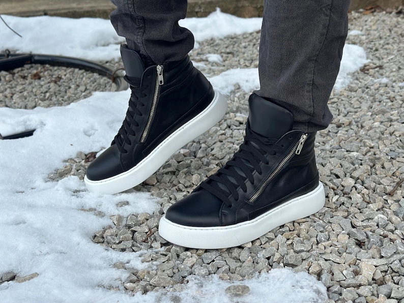 May include: A pair of black leather high-top trainers with white soles and a zip detail on the side.