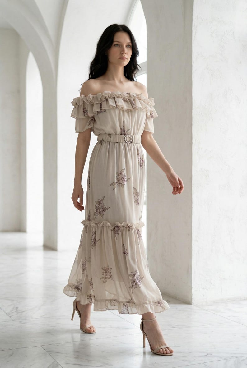 May include: A beige off-the-shoulder maxi dress with a floral pattern and a belted waist. The dress features ruffled detailing at the neckline and hem. The model is wearing nude high heels.