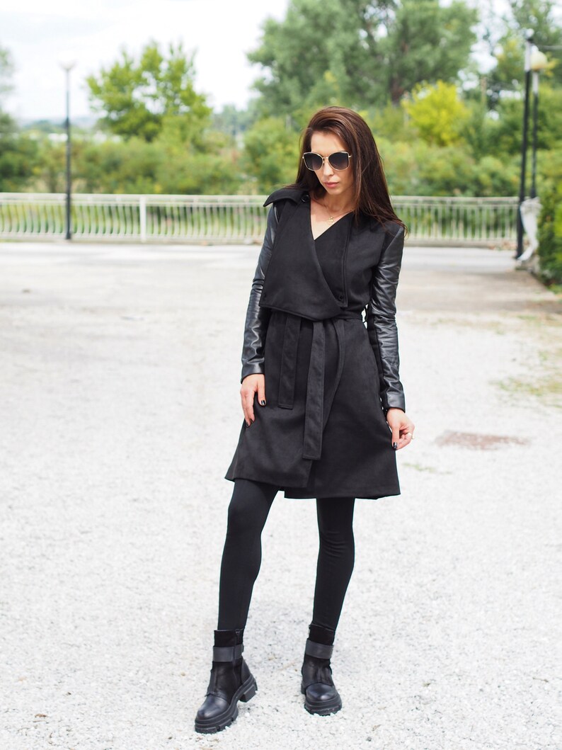 May include: A black wrap coat with leather sleeves and a belt. The coat is worn over black leggings and black ankle boots.