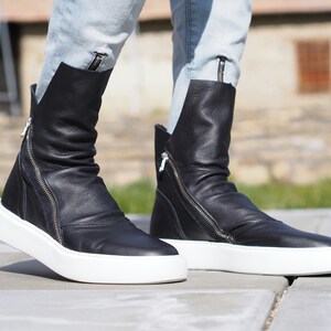 Puede incluir: Botas de tobillo de cuero negro con suela de plataforma blanca y cremallera lateral. Las botas son holgadas y tienen punta puntiaguda.
