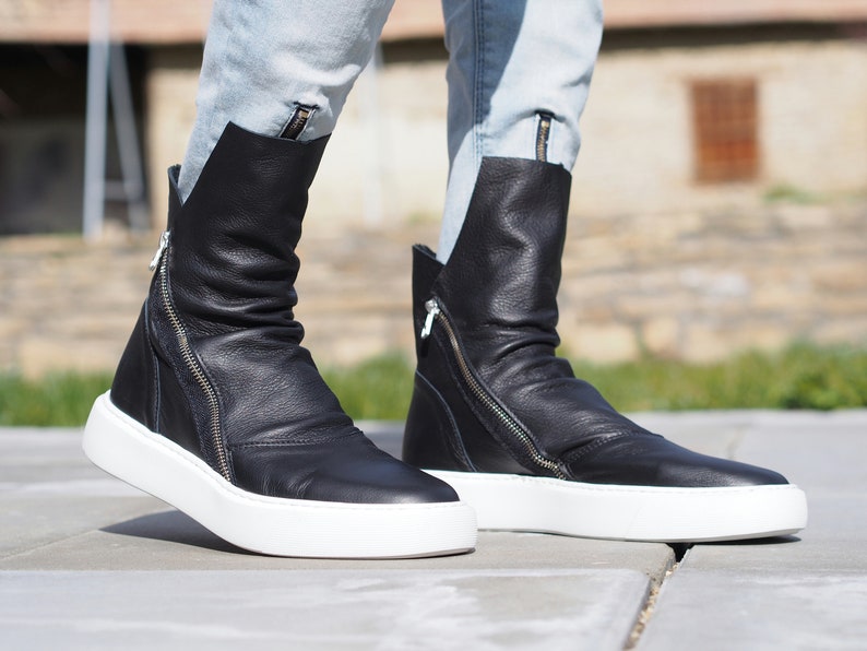 Puede incluir: Botas de tobillo de cuero negro con suela de plataforma blanca y cremallera lateral. Las botas son holgadas y tienen punta puntiaguda.
