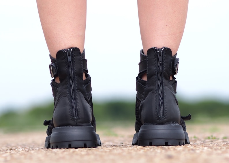 K&ouml;nnte beinhalten: Ein Paar schwarze Lederstiefel mit Rei&szlig;verschluss an der R&uuml;ckseite und einem Schnallenriemen. Die Stiefel haben einen dicken Absatz und eine Plateau-Sohle.