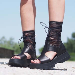 May include: Black leather platform sandals with a mesh upper and lace-up closure. The sandals have a chunky platform sole and an open toe design.