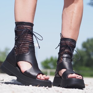 May include: Black leather platform sandals with a mesh upper and lace-up detail. The sandals have a chunky platform sole and an open toe design.