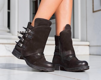 May include: Dark brown leather ankle boots with multiple buckles and silver-toned studs. The boots have a side zipper and a folded-over cuff. The soles are dark and slightly distressed, giving them a rugged appearance.