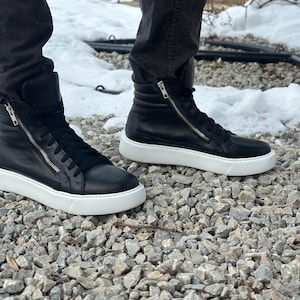 May include: A pair of black leather high-top trainers with white soles and a zip detail on the side.