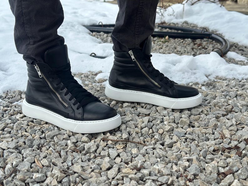 May include: A pair of black leather high-top trainers with white soles and a zip detail on the side.