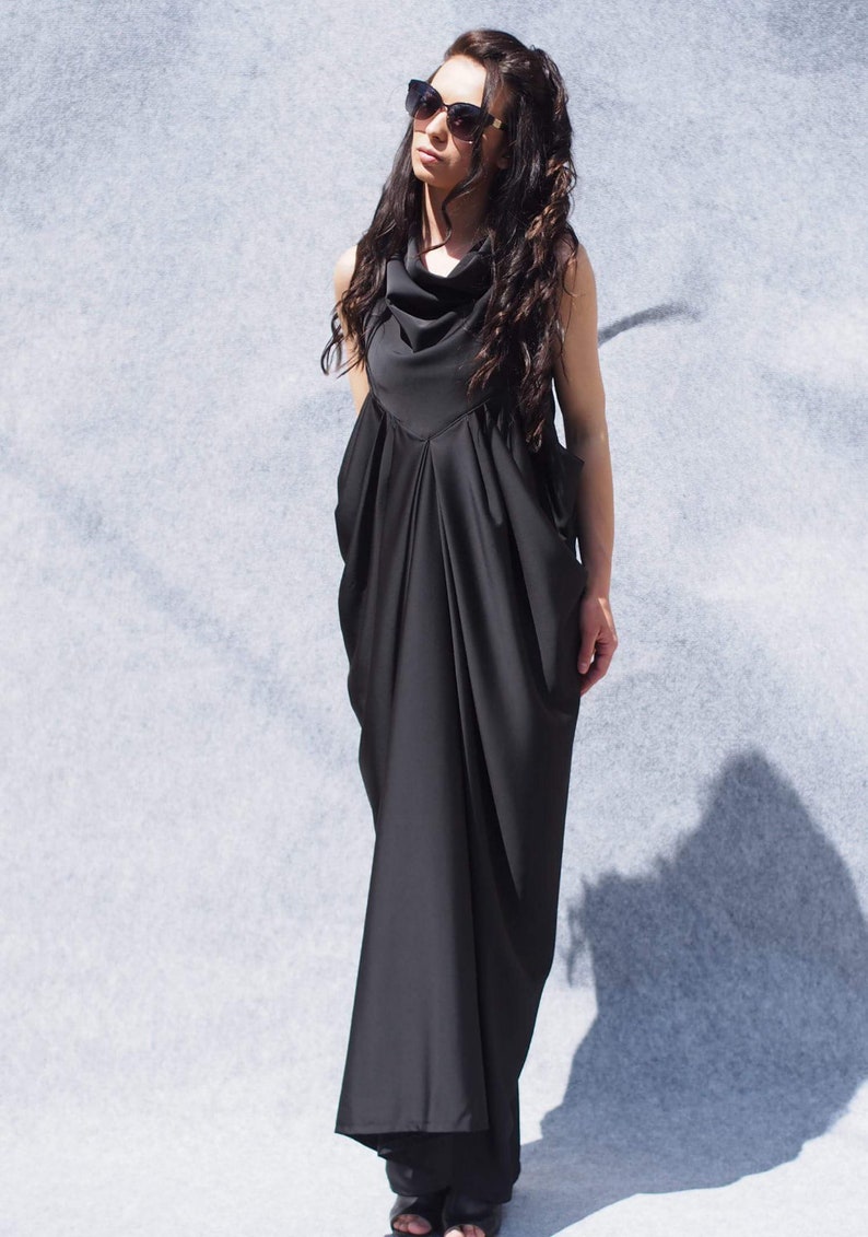 May include: A black maxi dress with a cowl neck and a flowing, draped skirt. The dress is sleeveless and has a relaxed fit.