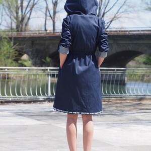 May include: A dark blue denim hooded jacket with a drawstring waist. The jacket has white text on the hem that reads "Your vibe attracts your tribe. The adventure begins your vibe."