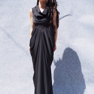 May include: A black sleeveless maxi dress with a cowl neck and a flowing, draped skirt. The dress is made of a soft, silky fabric and has a relaxed fit.