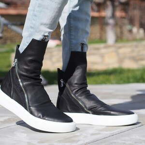 Puede incluir: Botas de tobillo de cuero negro con cremallera lateral y suela de plataforma blanca.