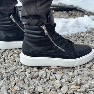 May include: Black leather high-top trainers with a white sole and a zip detail on the side.