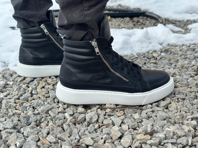 May include: Black leather high-top trainers with a white sole and a zip detail on the side.