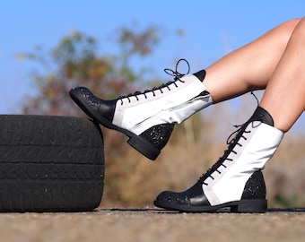May include: Black and white ankle boots with glitter accents and lace-up fastenings. The boots are being worn by a person sitting on a tyre.