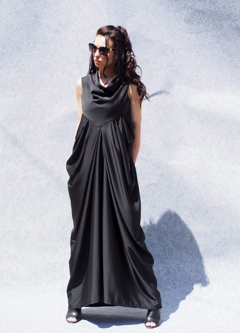 May include: A black sleeveless maxi dress with a cowl neck and a flowing, draped skirt. The dress is made of a soft, lightweight fabric.