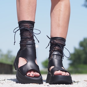 May include: Black leather platform sandals with a lace-up design and fishnet socks. The sandals have a chunky heel and an open toe.