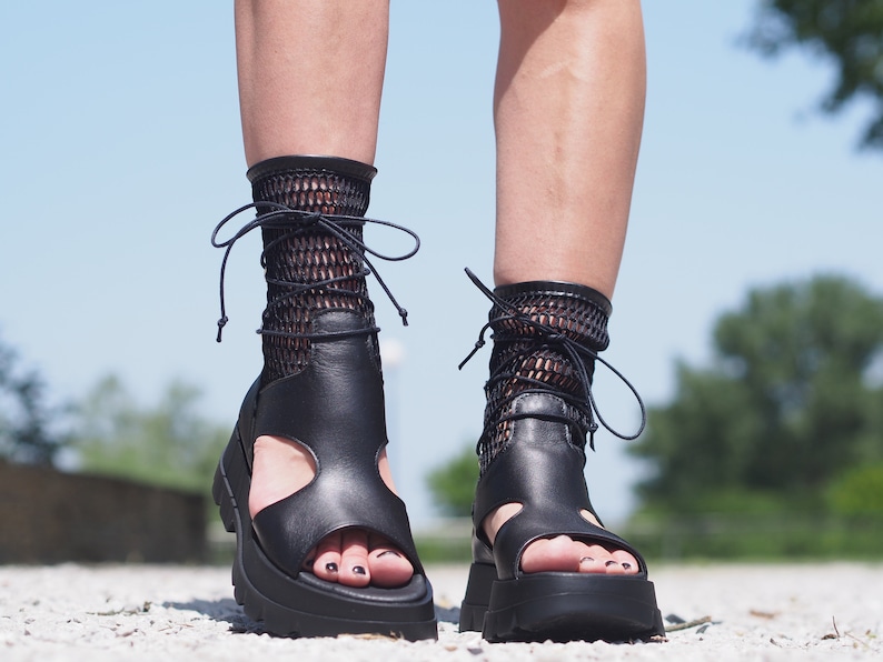 May include: Black leather platform sandals with a lace-up design and fishnet socks. The sandals have a chunky heel and an open toe.