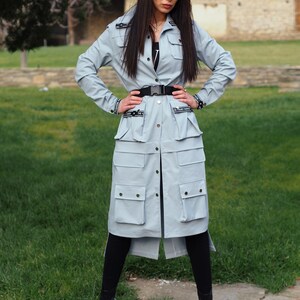 May include: A light blue long-sleeved jacket with a button-up front, multiple pockets, and a black belt. The jacket has black text that says "In Friend Fashion" on the front.