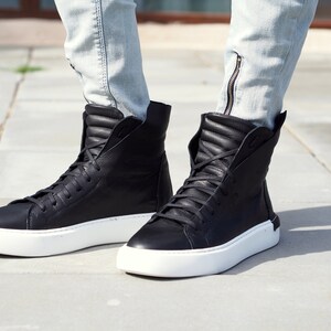May include: Black high-top sneakers with white soles. The sneakers have a zipper detail on the side and are made of leather.
