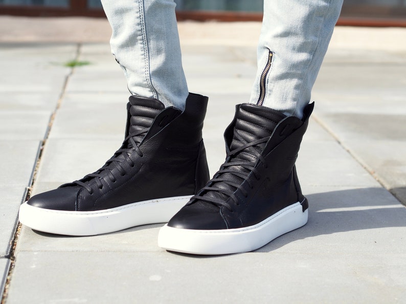 May include: Black high-top sneakers with white soles. The sneakers have a zipper detail on the side and are made of leather.