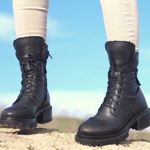 K&ouml;nnte beinhalten: Schwarze Leder-Stiefeletten mit Schn&uuml;rsenkeln und einem dicken Absatz. Die Stiefeletten haben ein strukturiertes Muster an der Spitze und einen Rei&szlig;verschluss an der Seite.