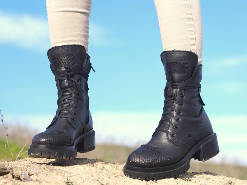 K&ouml;nnte beinhalten: Schwarze Leder-Stiefeletten mit Schn&uuml;rsenkeln und einem dicken Absatz. Die Stiefeletten haben ein strukturiertes Muster an der Spitze und einen Rei&szlig;verschluss an der Seite.