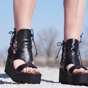 May include: Black leather platform sandals with lace-up detailing and an open toe design.