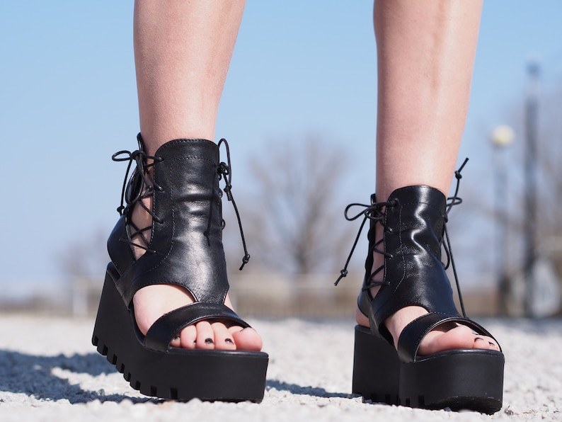 May include: Black leather platform sandals with lace-up detailing and an open toe design.