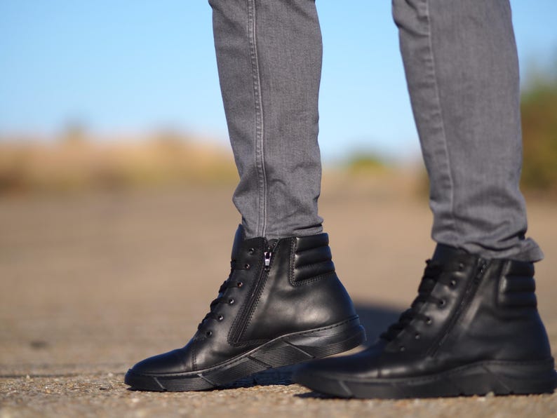 May include: Black leather ankle boots with a side zipper and lace-up closure. The boots have a ridged sole and are worn with gray denim jeans. The boots are a solid black color.