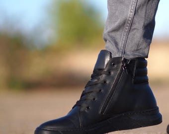 Puede incluir: Zapatillas altas negras con cremallera lateral y cordones. El zapato tiene una parte superior de cuero liso y una suela negra. El diseño incluye un cuello de tobillo acolchado y un panel de talón texturizado. Las zapatillas se usan con jeans grises.