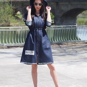 May include: A blue denim dress with a hood and a zipper closure. The dress has a drawstring waist and white text on the bottom hem that reads "Adventure Begins Your Vibe Attracts Your Tribe".