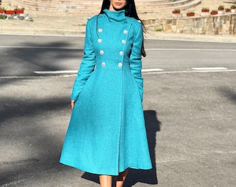 May include: A long-sleeved, knee-length teal coat featuring a high collar, a double-breasted front with two rows of silver-toned buttons, and a fitted waist that flares into a full skirt. The coat is made of a textured fabric.