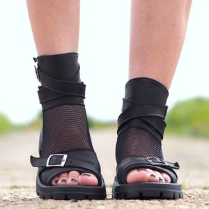 K&ouml;nnte beinhalten: Schwarze Ledersandalen mit einem Mesh-Einsatz und mehreren Riemen. Die Sandalen haben einen Schnallenverschluss und eine klobige Plateausohle.