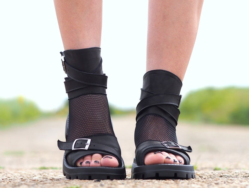 K&ouml;nnte beinhalten: Schwarze Ledersandalen mit einem Mesh-Einsatz und mehreren Riemen. Die Sandalen haben einen Schnallenverschluss und eine klobige Plateausohle.