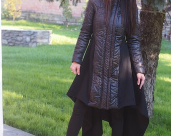 May include: A black asymmetrical coat with a high collar and a hood. The coat is quilted and has a shiny finish. The model is wearing black leggings and black boots.