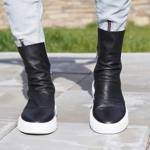 Puede incluir: Un par de botines de cuero negro con suela de plataforma blanca. Las botas tienen una cremallera lateral y una punta puntiaguda.