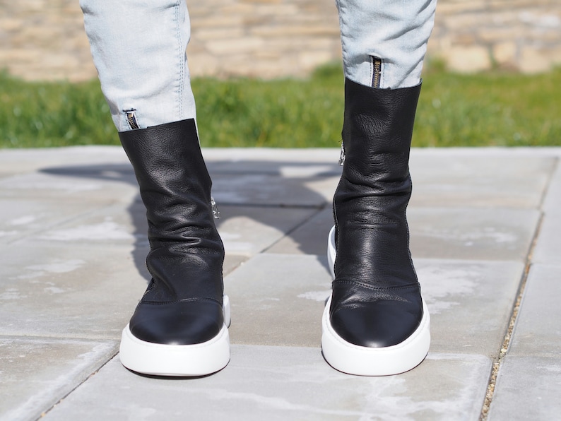 Puede incluir: Un par de botines de cuero negro con suela de plataforma blanca. Las botas tienen una cremallera lateral y una punta puntiaguda.