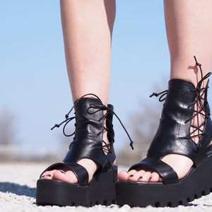 May include: Black leather platform sandals with lace-up detailing and a chunky heel.