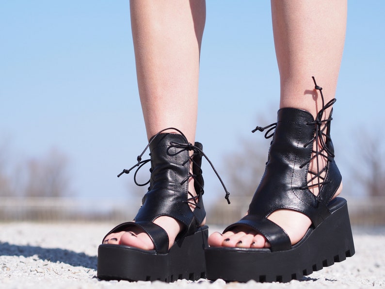 May include: Black leather platform sandals with lace-up detailing and a chunky heel.