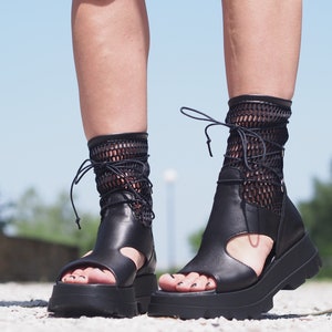 May include: Black leather platform sandals with a mesh ankle strap and lace-up closure. The sandals have a chunky platform sole and an open toe design.