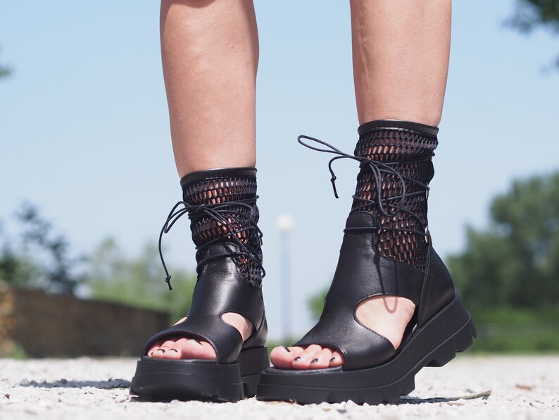 May include: Black leather platform sandals with a mesh ankle strap and lace-up closure. The sandals have a chunky platform sole and an open toe design.