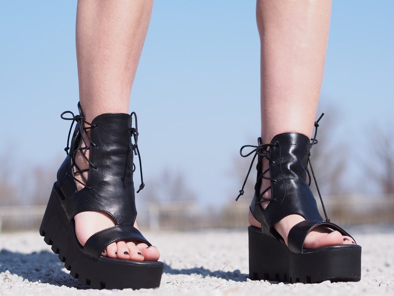 May include: Black leather platform sandals with lace-up detailing and a chunky platform sole.
