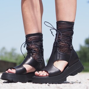 May include: Black leather platform sandals with a mesh upper and lace-up closure. The sandals have a chunky platform sole and an open toe design.