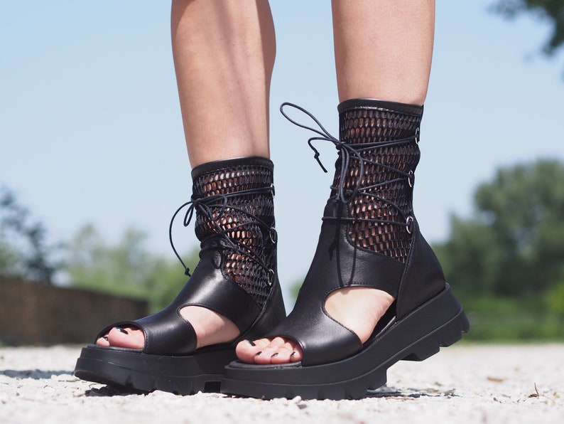 May include: Black leather platform sandals with a mesh upper and lace-up closure. The sandals have a chunky platform sole and an open toe design.