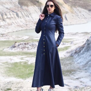 May include: A long, dark blue denim dress with a button-up front and a collared neckline. The dress has a flared skirt and is worn with white sneakers.