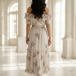May include: An off-the-shoulder midi dress in a light cream color featuring a dark floral print. The garment includes a ruffled neckline, an elasticized waist, and a tiered skirt with a ruffled hemline, viewed from the back.
