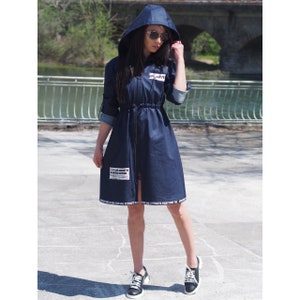 May include: A dark blue denim hooded jacket with a zipper closure and a drawstring waist. The jacket has white text on the front and bottom hem.