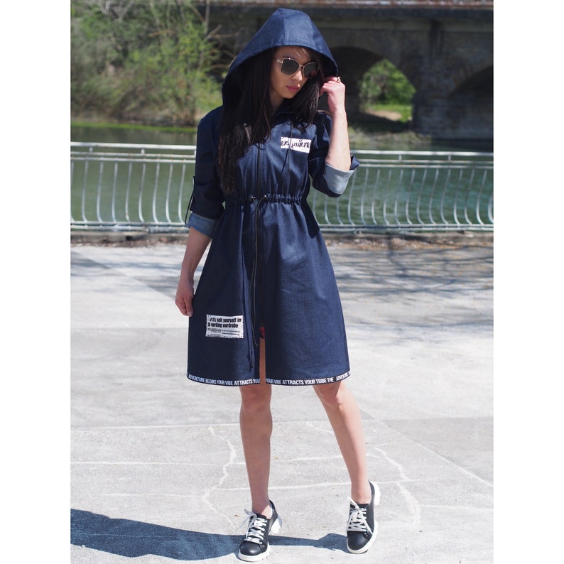 May include: A dark blue denim hooded jacket with a zipper closure and a drawstring waist. The jacket has white text on the front and bottom hem.