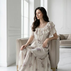 May include: A cream-colored dress with a floral pattern and a belted waist. The dress features short sleeves, ruffles, and a flowing skirt. The woman is wearing silver high heels.
